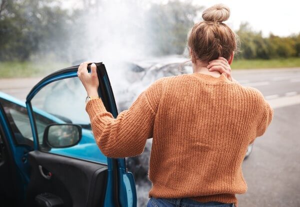 Woman clutching her neck and exiting a car after having an accident on a highway