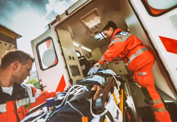 A male and a female paramedic helping a patient on a stretcher into an ambulance