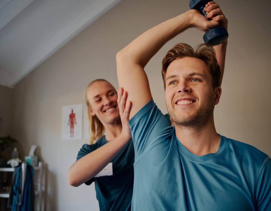 Man smiling with a dumbell while a smiling female nurse helps him