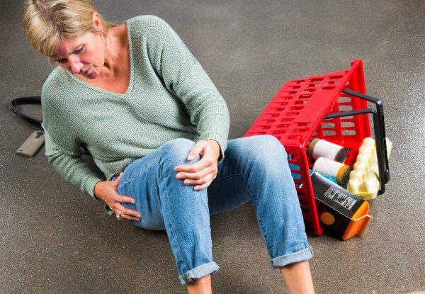 Woman lying on the floor clutching her knee in pain with dropped shopping basket beside her