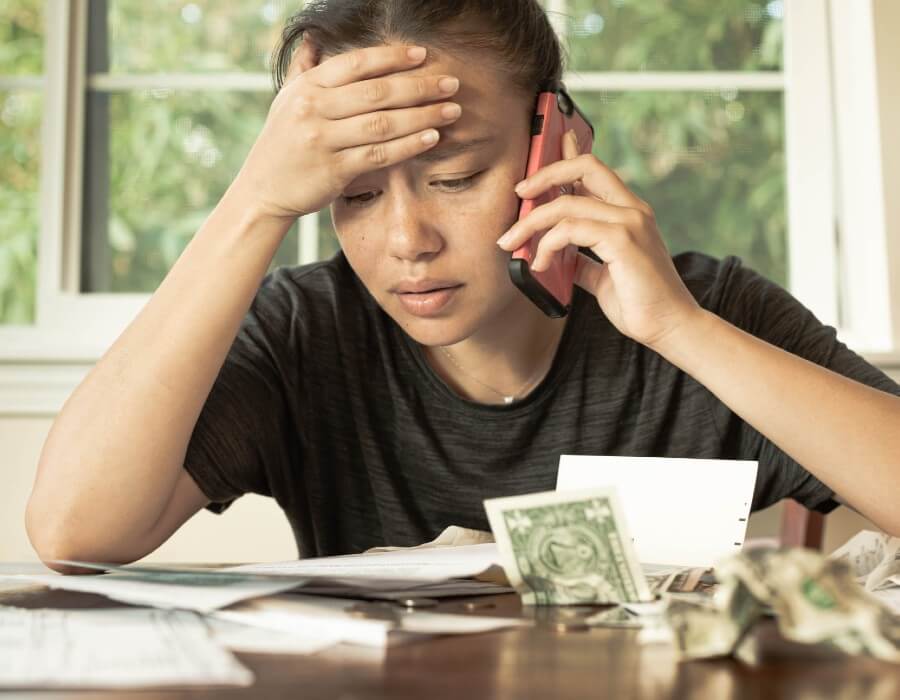 Troubled woman speaking on cell phone with crumpled dollar bills in front of her