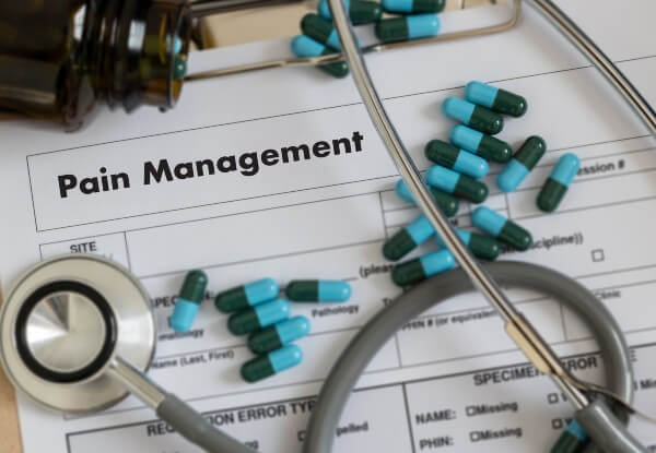 A pain management form with stethoscope and pills scattered on top of it